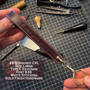 May include: Burgundy leather keychain with gold hardware and white stitching. The keychain is engraved with the text "Love you more". #8 Burgundy CXL Size Large Type C Keychain Font B36 White Stitching Gold Finish Hardware