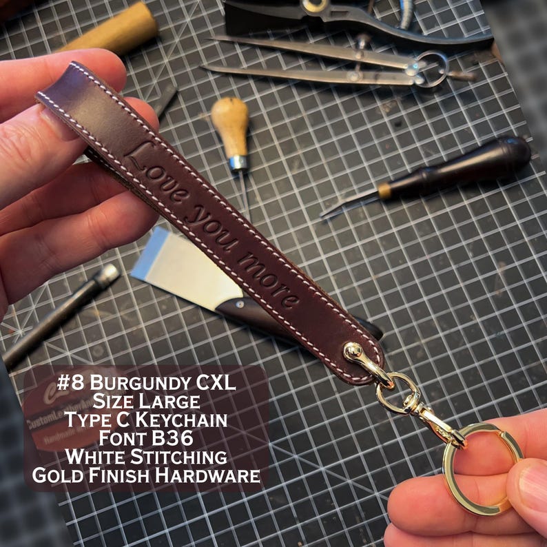 May include: Burgundy leather keychain with gold hardware and white stitching. The keychain is engraved with the text "Love you more". #8 Burgundy CXL Size Large Type C Keychain Font B36 White Stitching Gold Finish Hardware