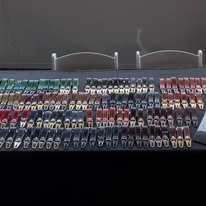 May include: A display of leather belts in various colors, including red, green, black, and brown, with silver-colored buckles. The belts are arranged on a black table, showcasing a wide selection of styles and hues.
