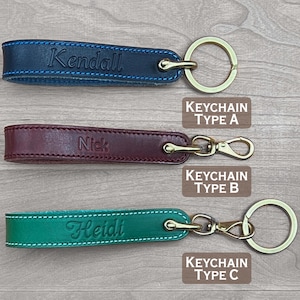 Three handmade personalized leather keychains with different styles.  The top keychain is blue leather with 'Kendall' embroidered in blue thread, featuring a beautiful brass shackle and matching keyring. The middle keychain is burgundy leather with 'Nick' embossed with a removable shackle and lever clasp. The bottom keychain is green leather with 'Heidi' engraved, and has a removable brass shackle with key ring and lever snap clasp. Each keychain is handmade to order by CustomLeatherAndPen