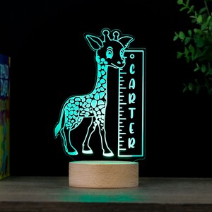 May include: A turquoise blue giraffe night light with a wooden base. The giraffe is holding a ruler with the name "Carter" on it.