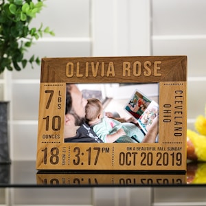 May include: A wooden photo frame with a picture of a father reading to his baby. The frame has the baby's name "Olivia Rose" and birth details: 7 lbs 10 oz, 18 1/2 inches, 3:17 PM, Oct 20, 2019, Cleveland, Ohio.