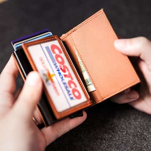 May include: A brown leather wallet with a Costco Wholesale membership card inside. The wallet is open and there is a bill of cash inside.