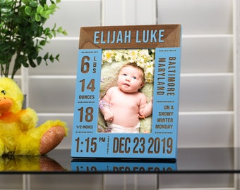 May include: A blue wooden photo frame with a brown border. The frame has a photo of a baby in it, and the text "ELIJAH LUKE" is printed at the top. The frame also includes the baby's birth information: 6 lbs, 14 ounces, 18 1/2 inches, 1:15 PM, DEC 23 2019, BALTIMORE MARYLAND, ON A SNOWY WINTER MONDAY.