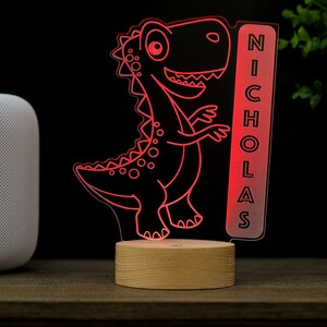 May include: Red dinosaur night light with a wooden base and a clear acrylic panel with the name "NICHOLAS" on it.