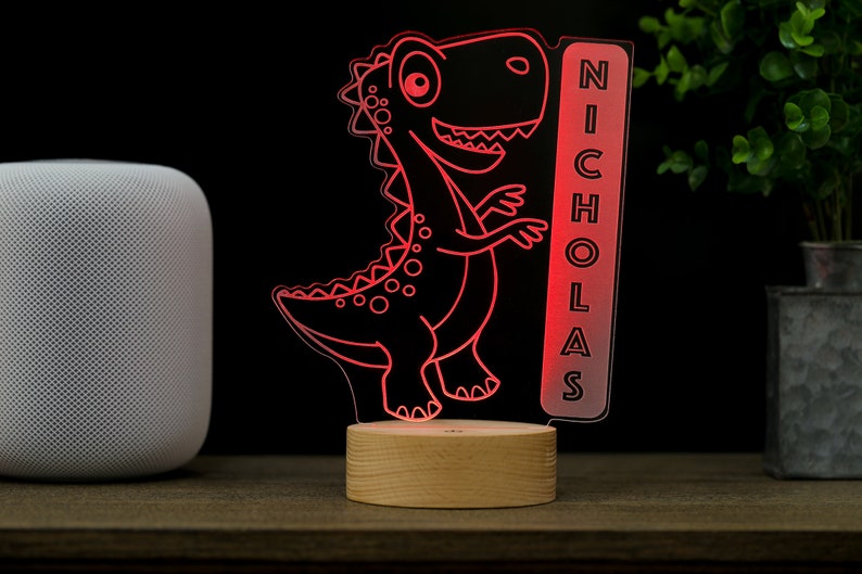 May include: Red dinosaur night light with a wooden base and a clear acrylic panel with the name "NICHOLAS" on it.
