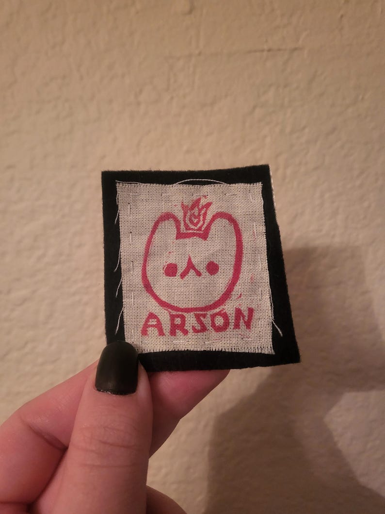 May include: A black and white patch with a red cartoon animal with a flame on its head. The text "ARSON" is printed below the animal.