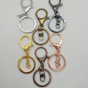 May include: Five keyrings in different colours: silver, bronze, gold, rose gold, and black. Each keyring has a round ring and a swivel clasp.