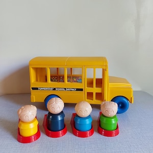 May include: A yellow plastic school bus toy with blue wheels and the text "Tuppertoys School District." Four small figures with different coloured tops are in front of the bus. The figures are on red bases.