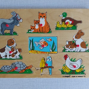 Op de afbeelding: Houten dierenpuzzel met een ezel, kattenfamilie, eend met kuikens, hond met puppy's, vis, konijn met konijntjes, schildpad, parkieten en een kip met kuikens. De puzzelstukken hebben rode knoppen.