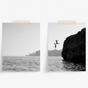 Może przedstawiać: Dwie osoby skaczą z klifu do oceanu. Klif znajduje się po prawej stronie obrazu, a ocean po lewej. Niebo jest szare, a woda spokojna.