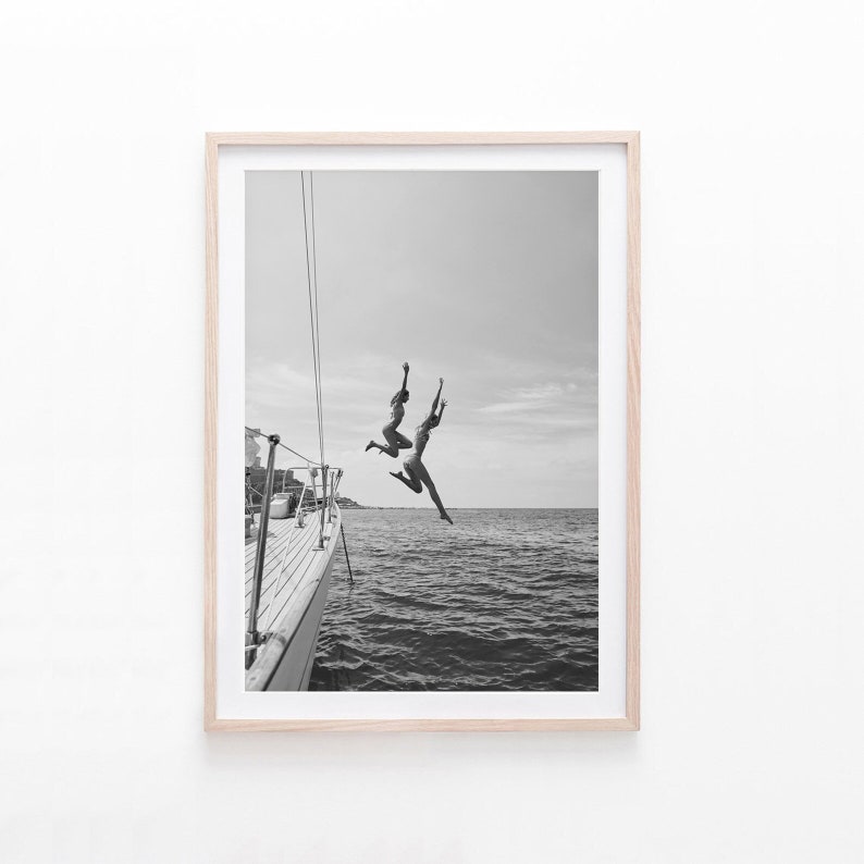 May include: Two people jump off the back of a boat into the water. The boat is docked and the water is calm. The photo is in black and white.