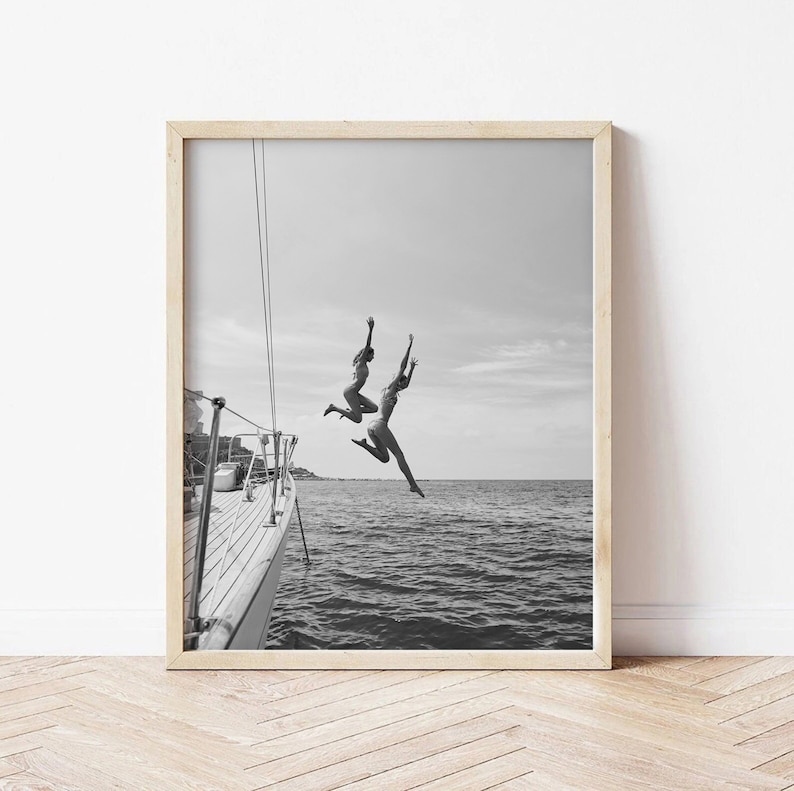 May include: Black and white photograph of two people jumping off a boat into the ocean. The boat is in the foreground and the ocean is in the background.