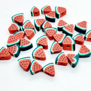 May include: A collection of red, green, and black watermelon slice-shaped beads. Each bead has a hole for stringing and features black seed details. The beads are scattered on a white surface.