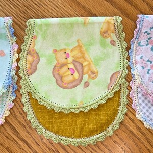 May include: Three baby bibs with scalloped edges and colorful patterns. One bib features a blue background with animal faces, another has a green background with bears, and the third has a pink floral design.