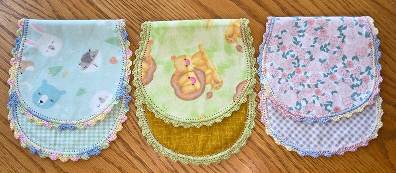 May include: Three baby bibs with scalloped edges and colorful patterns. One bib features a blue background with animal faces, another has a green background with bears, and the third has a pink floral design.