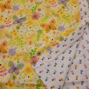 May include: A yellow baby blanket with a floral pattern featuring butterflies and flowers. The reverse side of the blanket is white with a small floral pattern.