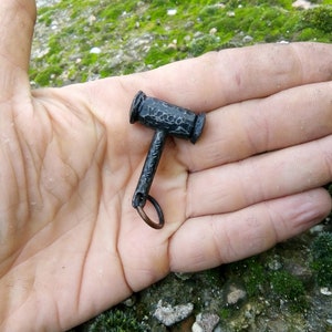 May include: A small black metal hammer keychain with a ring attached. The hammer has a textured surface and a rounded head.