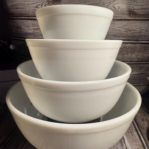 Peut inclure: Une pile de quatre saladiers blancs de tailles différentes. Les bols sont emboîtés les uns dans les autres, le plus grand en bas et le plus petit en haut. Les bols ont un design simple et arrondi.