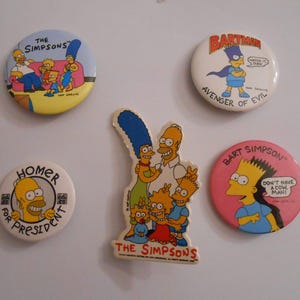 May include: A collection of The Simpsons character pins and a magnet. The pins feature Homer, Bart, and the whole family. One pin reads "Homer for President." Another features Bart as "Bartman, Avenger of Evil."