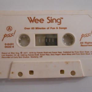 May include: An off-white cassette tape with the title "Wee Sing" and the text "Over 60 Minutes of Fun & Songs." The tape features the text "pss!" and "All Rights Reserved." The cassette has a rectangular window.