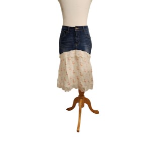 May include: A denim skirt with a white lace overlay. The skirt features a high waist and a mid-length design. The lace overlay is patterned with small, orange-colored flamingo designs.