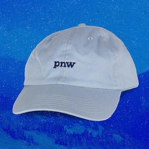 May include: A light blue baseball cap with the embroidered letters "pnw" in navy blue. The cap has a curved brim and a fabric strap closure. The hat is made of a soft, durable material.