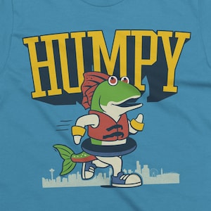 May include: A light blue t-shirt featuring a cartoon fish character wearing a life vest and inner tube, running. The word "HUMPY" is printed in yellow block letters above the fish. A cityscape is visible at the bottom.