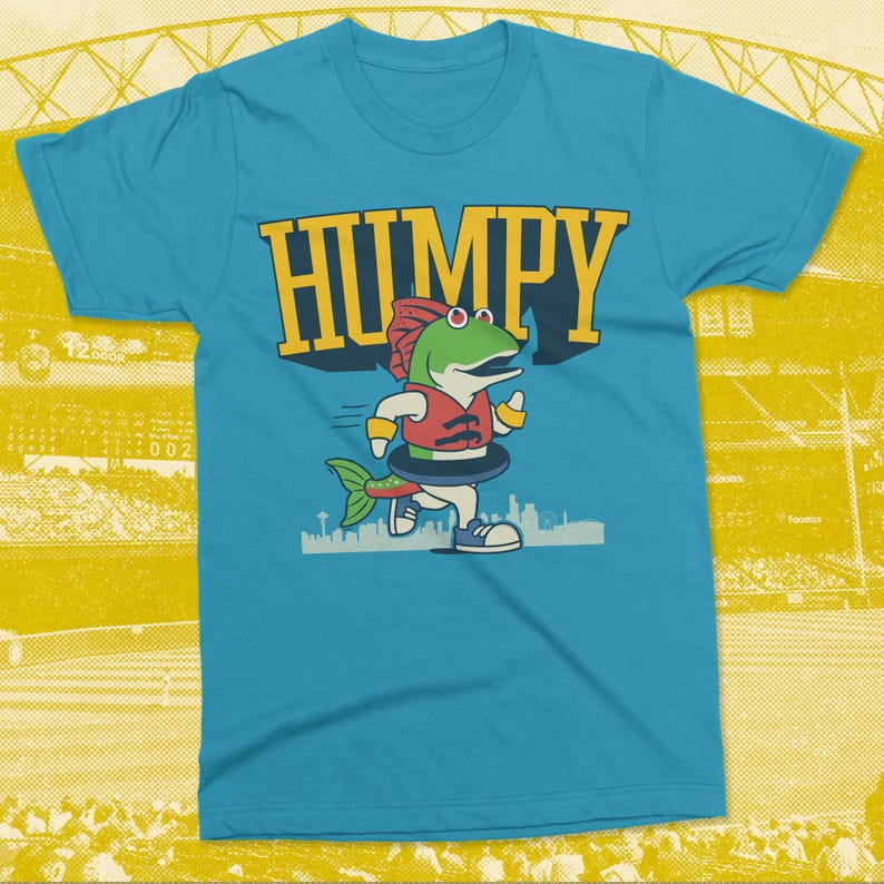 May include: A turquoise t-shirt featuring a cartoon fish character wearing a life vest and inner tube, running in front of a city skyline. The word "HUMPY" is printed in large yellow letters above the fish.