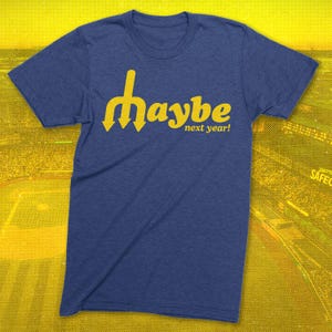 May include: A navy blue t-shirt with the yellow text "Maybe next year!" The word "Maybe" is stylized with a unique font and arrow design. The shirt is made of a soft material and is suitable for casual wear.