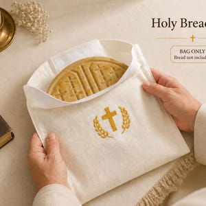May include: A cream-colored Holy Bread Bag with a gold embroidered cross and wheat design. The bag holds a round, textured bread. Text on the image reads "Holy Bread Bag" and "BAG ONLY Bread not included".