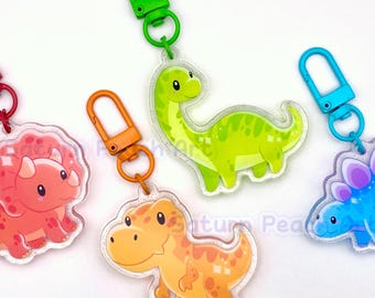 May include: Four colorful dinosaur-shaped keychains. The keychains feature a red triceratops, an orange T-Rex, a green Brontosaurus, and a blue Stegosaurus. Each keychain has a different colored clasp: red, orange, green, and blue.
