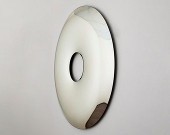 May include: A large, round, silver-colored wall mirror with a circular hole in the center. The mirror is slightly convex, giving it a slightly distorted reflection.