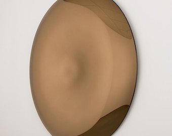 May include: A large, oval-shaped wall mirror with a bronze-colored, reflective surface. The mirror has a slightly irregular shape and is mounted on a white wall. The bronze color gives the mirror a warm, inviting appearance.