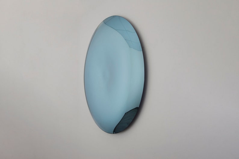 Puede incluir: Un espejo grande, ovalado, de color azul con un reflejo ligeramente distorsionado.