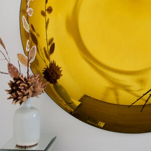 Pode incluir: Um espelho redondo dourado com um arranjo decorativo de flores secas em um vaso branco na frente dele.