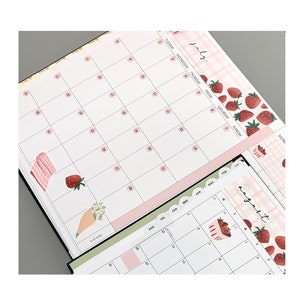 May include: A pink and white monthly planner with a strawberry and gingham pattern. The planner has tabs for each month of the year and includes a to-do list section.