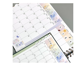 Op de afbeelding: Een maandplanner met een bloemenontwerp. De planner heeft tabbladen voor elke maand, en de huidige maand is mei. De planner heeft ook een sectie voor dagelijkse notities en een sectie voor wekelijkse notities.