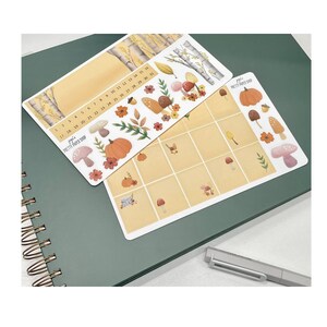 May include: Two sheets of stickers with a fall theme. The first sheet has a calendar with numbers 1-31, a pumpkin, mushrooms, leaves, and trees. The second sheet has a grid of squares with mushrooms, leaves, and a pumpkin. The text "juju's pretty paper shop" is on both sheets.