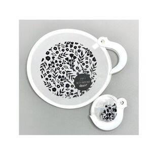 Op de afbeelding: Witte, ronde handventilator met een zwart bloemenpatroon en een witte handgreep. De ventilator heeft de tekst "jojo's PRETTY PAPER SHOP". Een kleinere, bijpassende ventilator is ook aanwezig.