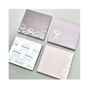 May include: Four square Post-it notes in shades of gray and pink. Two notes have white floral designs, one with a border of flowers and the other with a single flower. The fourth note has the Post-it brand logo.