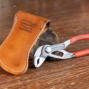 May include: A brown leather tool holder with the text "CRAFTED BY NC LASER CO" and a silhouette of the United States. A red and silver Knipex Cobra pliers is next to the holder.