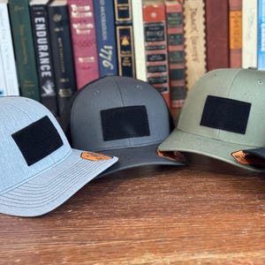 May include: Three trucker hats with black mesh back panels and black velcro patches. The hats are in gray, green, and light blue.