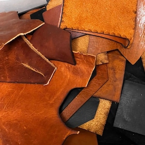May include: A collection of brown leather scraps in various shapes and sizes. The leather is a mix of light and dark brown shades.