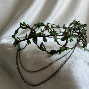 May include: A green leaf crown with a chain detail. The crown is made of faux leaves and berries and has a delicate chain attached to the back.
