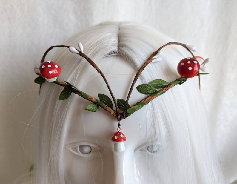 May include: A woodland-themed crown with brown branches, green leaves, and red and white mushroom accents.