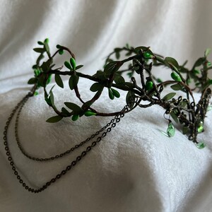 May include: A green leaf crown with a delicate wire frame and dangling chains. The crown is adorned with small green leaves and beads.