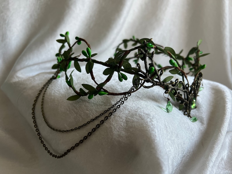 May include: A green leaf crown with a delicate wire frame and dangling chains. The crown is adorned with small green leaves and beads.