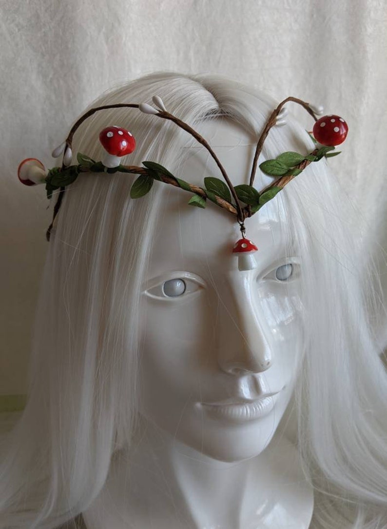 May include: A white headband with brown branches, green leaves, and red and white mushroom accents.