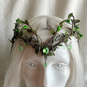 May include: A green and gold leaf crown with green gem accents. The crown is made of metal and has a delicate, intricate design.